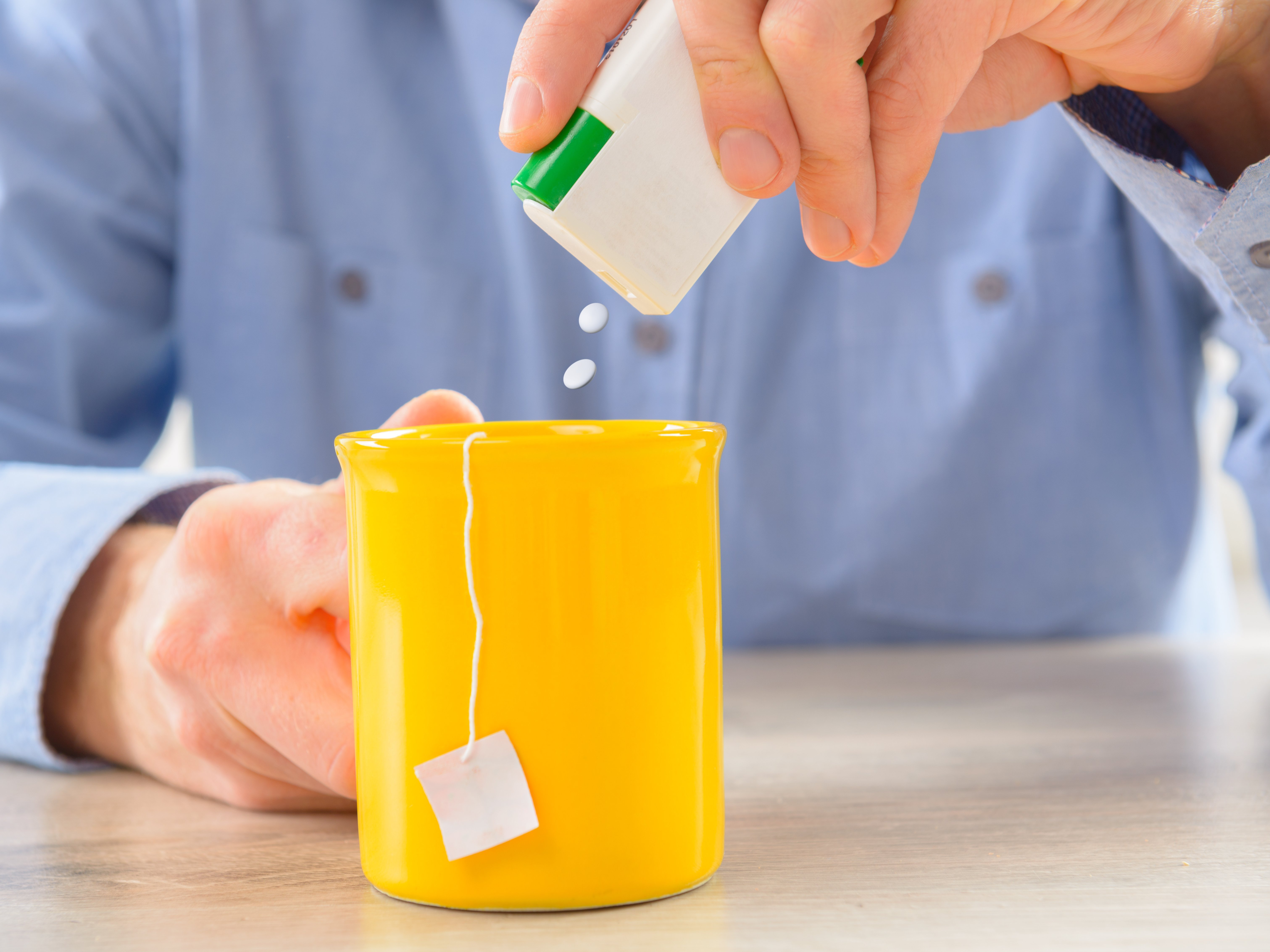 Mann in blauem Hemd süßt mit 2 Stück Süßstoff Sorbit seinen Tee in gelber Tasse